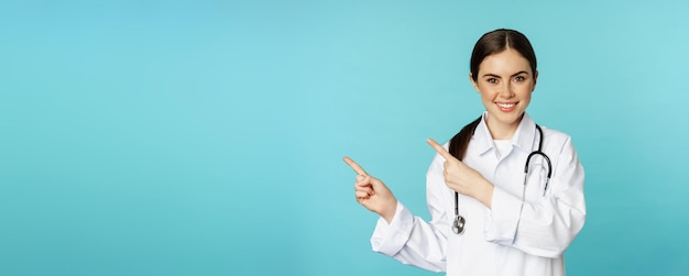 Free Photo portrait of smiling medical worker girl doctor in white coat with stethoscope pointing fingers left