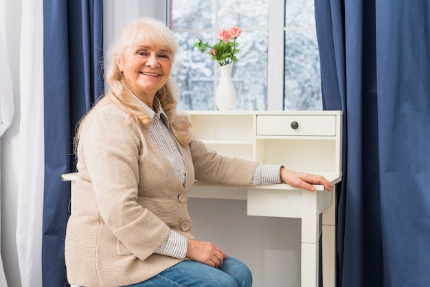 Portrait of a smiling senior woman sitting in front of window near the desk