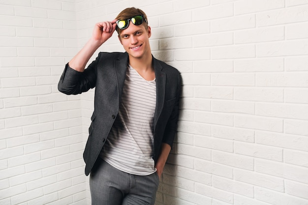 Free photo portrait of smiling stylish man standing against brick wall in modern office