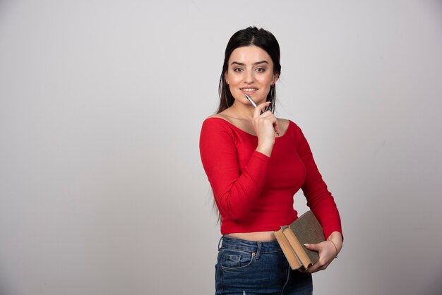 Portrait of a smiling woman holding two books and pencil.