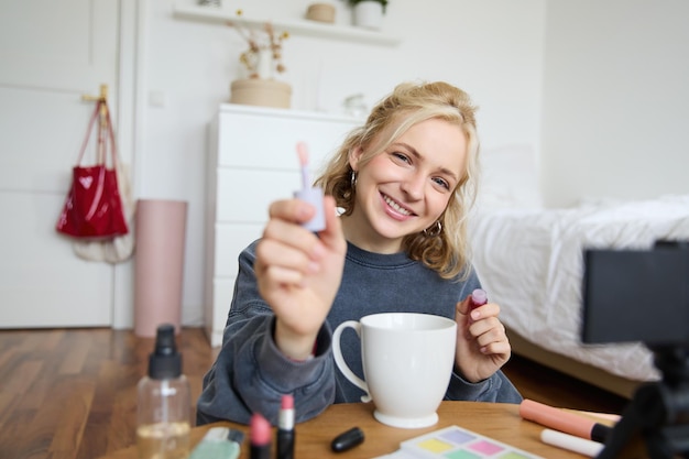 Free photo portrait of smiling woman shows lip gloss advertising makeup on her social media account recording