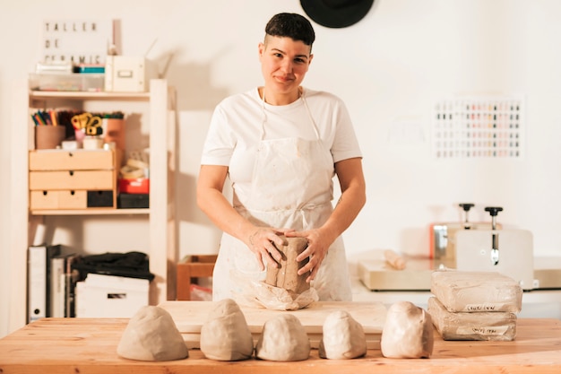 Portrait of a smiling woman with kneaded clay in the workshop