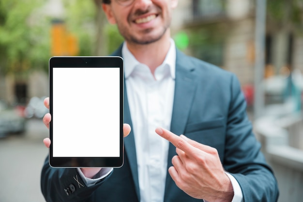 Free photo portrait of a smiling young businessman pointing his finger toward the digital tablet