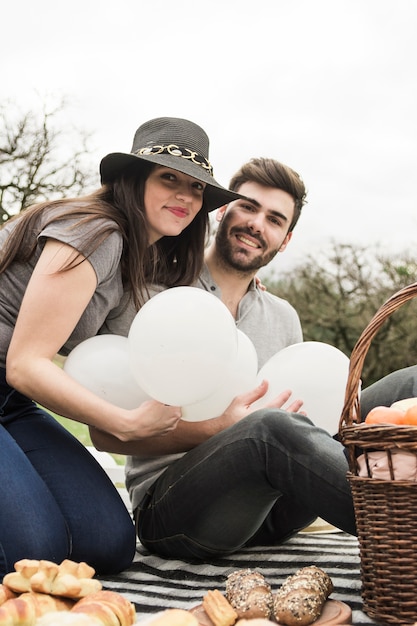 Portrait of smiling young couple holding white balloons at picnic