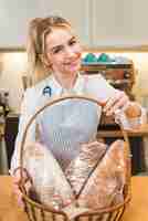 Free photo portrait of a smiling young female baker giving loaves of bread in the basket