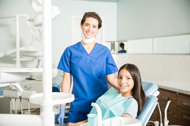 Portrait of smiling young female dentist standing by teenage girl in clinic