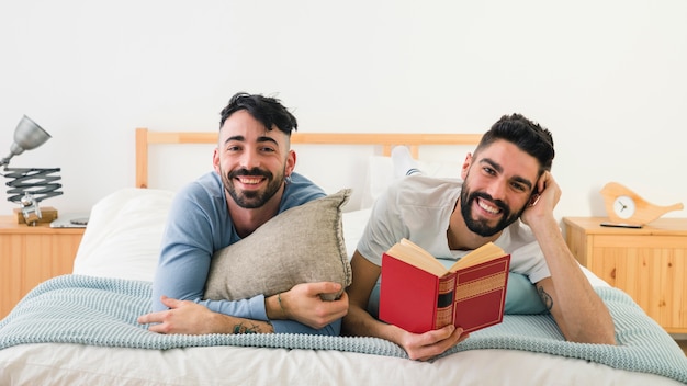 Portrait of smiling young homosexual couple lying on front over the bed looking at camera