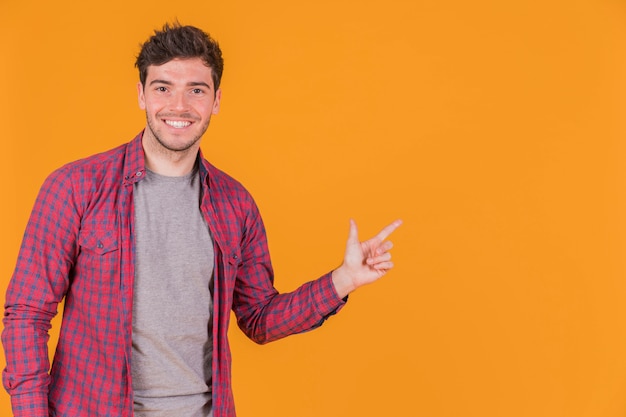 Portrait of a smiling young man pointing his finger on an orange background