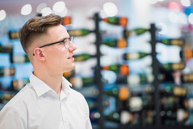 Free photo portrait of a smiling young man standing in front of arranged bar bottles