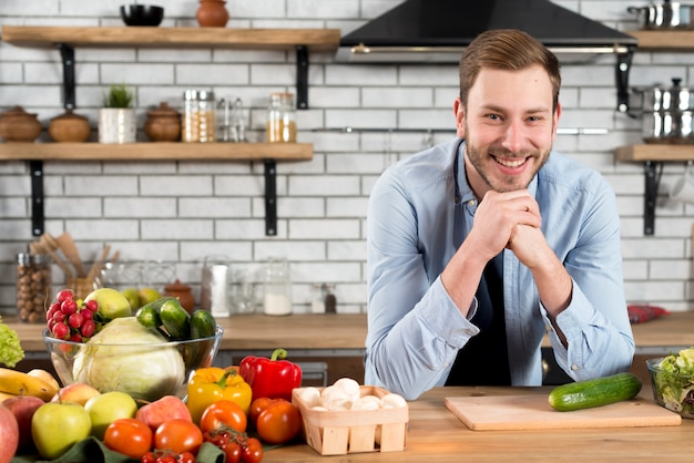 Portrait of a smiling young man with colorful vegetables on table in the kitchen