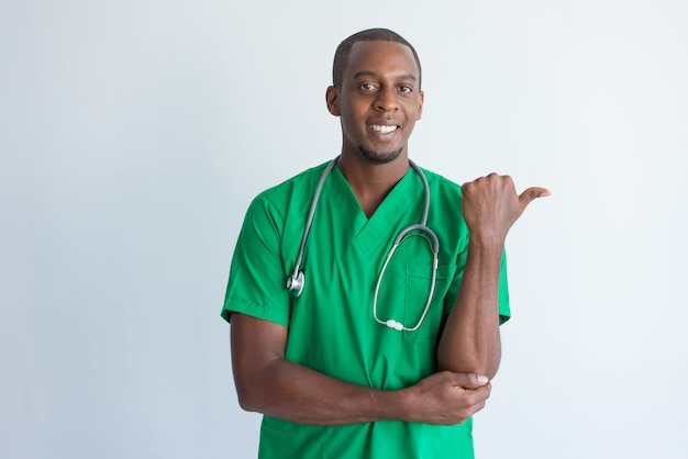 Free photo portrait of smiling young physician pointing at something with thumb.