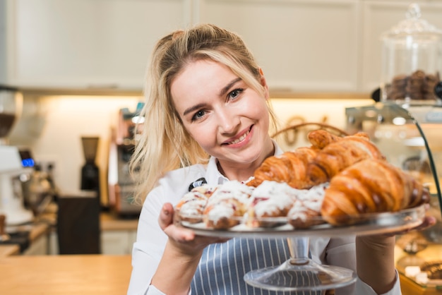 Portrait of a smiling young woman holding baked croissant on the cake stand