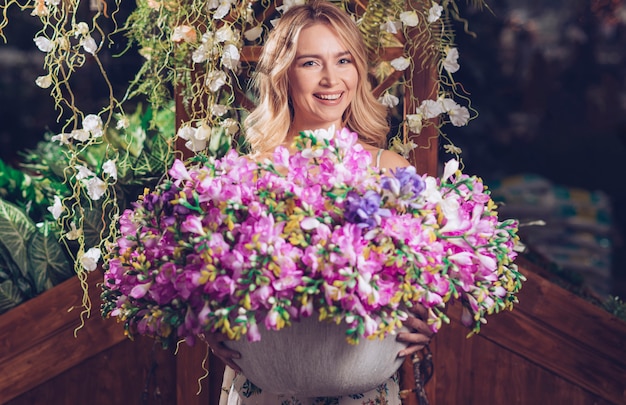 Portrait of a smiling young woman holding colorful flower vase in hand