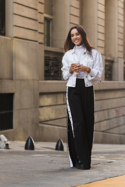 Portrait of a smiling young woman holding disposable coffee cup in hand