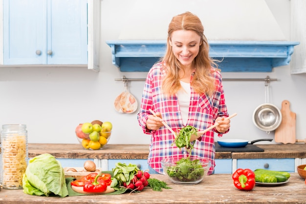 Free Photo portrait of a smiling young woman holding fresh spinach with wooden spoon