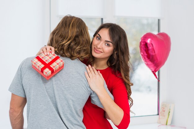 Portrait of a smiling young woman holding red gift box embracing her boyfriend