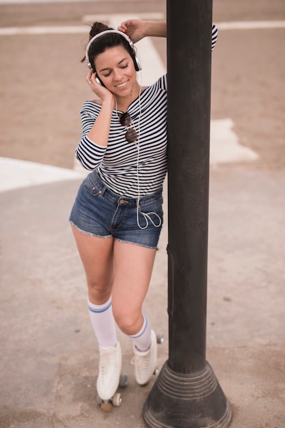 Free photo portrait of a smiling young woman listening music on headphone standing near the pillar