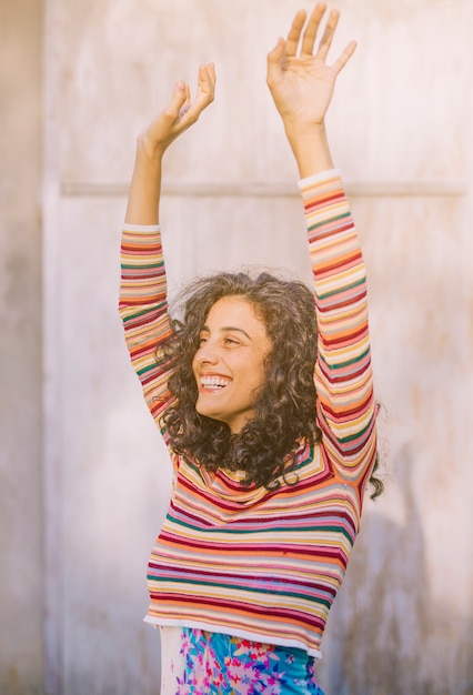 Free photo portrait of a smiling young woman raising her arms against wall