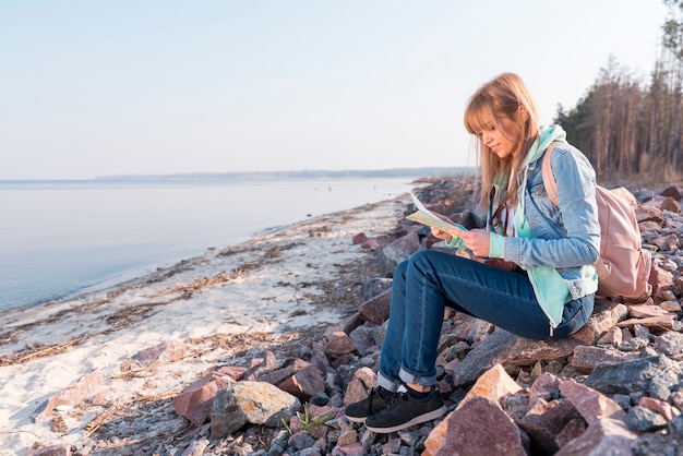 Free photo portrait of a smiling young woman sitting on beach looking at map