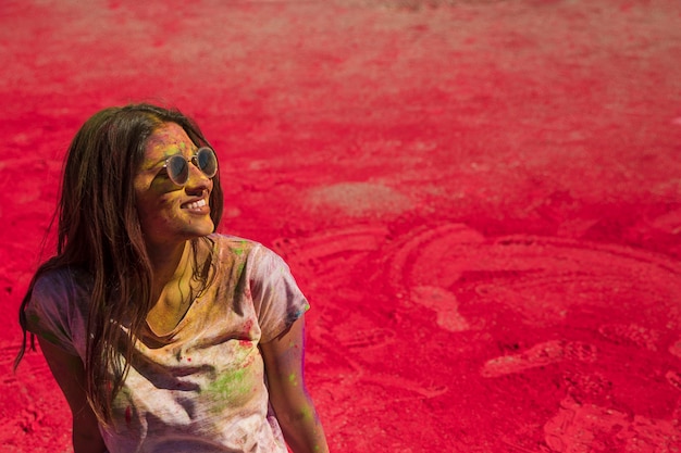 Portrait of a smiling young woman wearing sunglasses messing in holi color