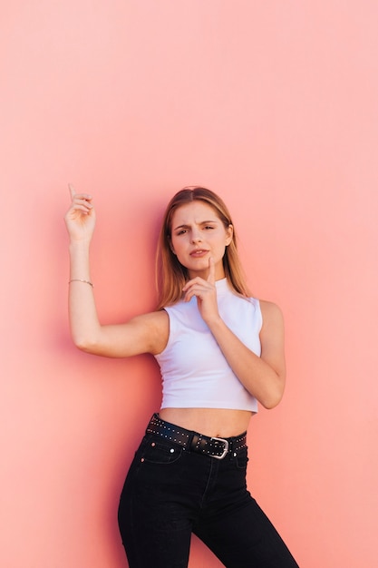 Portrait of a smiling young woman with finger on her chin pointing finger against peach background