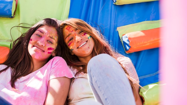 Free Photo portrait of a smiling young women with holi color paint on their face looking at camera