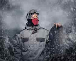 Free photo portrait of a snowboarder dressed in a full protective gear for extream snowboarding posing with snowboard against the background of mountains