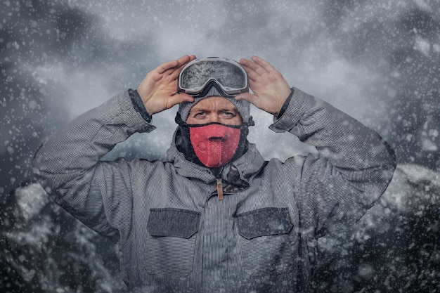 Free photo portrait of a snowboarder dressed in a full protective gear for extream snowboarding puts on glasses while standing against the background of mountains.