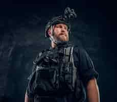 Free photo portrait of a special forces soldier wearing body armor and helmet with a night vision. studio photo against a dark textured wall