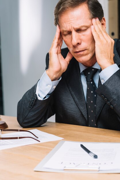 Portrait of stressed mature lawyer touching his head in the office