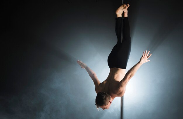 Portrait of strong male model performing a pole dance