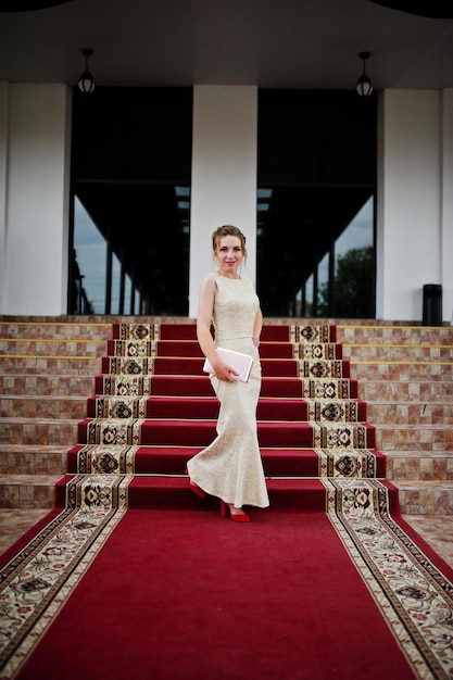 Free photo portrait of a stunning young woman in pretty evening gown posing on the carpet indoors