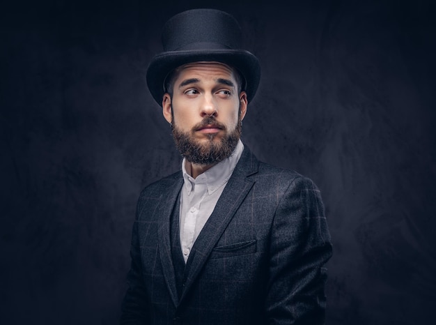 Free photo portrait of a stylish bearded male in an elegant suit and cylinder hat, over dark background.