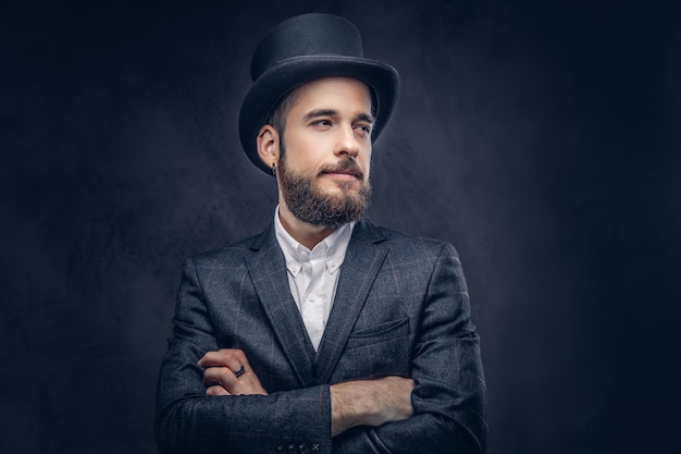 Free photo portrait of a stylish bearded male in an elegant suit and cylinder hat, over dark background.