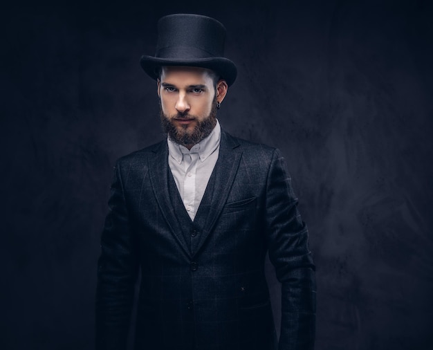 Free photo portrait of a stylish bearded male in an elegant suit and cylinder hat, looking at a camera over dark background.