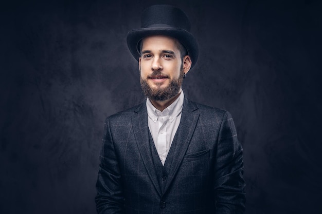 Free photo portrait of a stylish bearded male in an elegant suit and cylinder hat, looking at a camera over dark background.