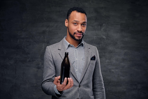 Free photo portrait of stylish black american male dressed in a grey suit holds a craft beer bottle.