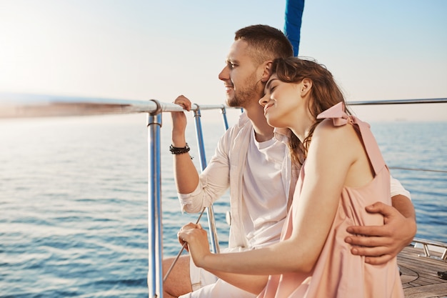 Free Photo portrait of stylish couple in love, hugging while sitting on bow of private yacht and enjoying view of sea. husband took his wife to beautiful warm country, celebrating honeymoon