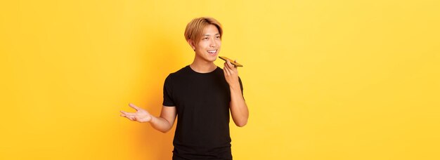 Free photo portrait of stylish handsome korean guy with blond hair record voice message on mobile phone holding