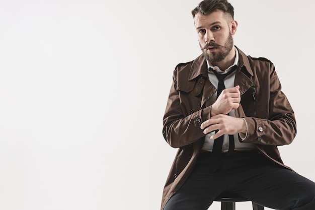 Free photo portrait of stylish handsome young man sitting at studio against white.