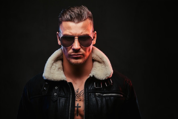 Free photo portrait of a stylish man in jeans jacket with dark glasses and stylish hair on a dark background.