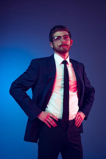 Portrait of stylish man with moustache wearing official suit posing isolated over blue studio background in neon light