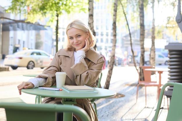 Free Photo portrait of stylish modern woman sitting in an outdoor cafe smiling and drinking coffee from