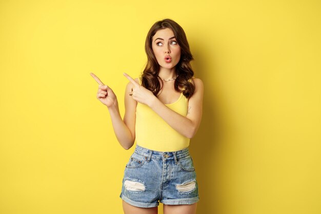 Portrait of stylish summer girl brunette woman showing way pointing fingers left advertising standin...