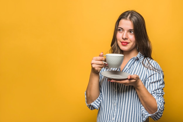 Portrait of a stylish young woman holding cup in hands looking away