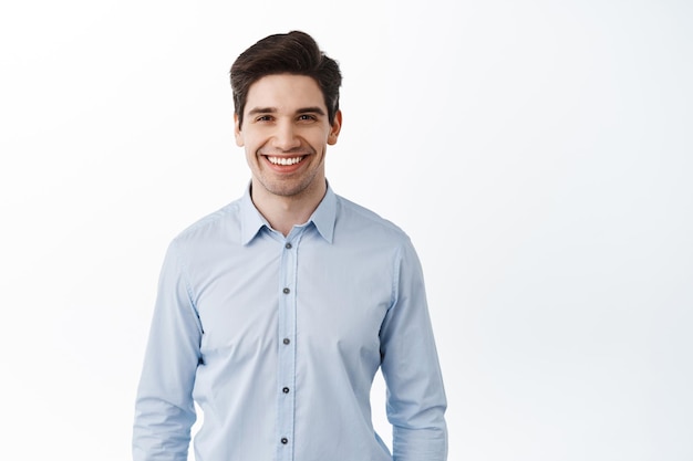 Portrait of successful businessman, happy office worker ceo smiling pleased, standing against white background in blue collar shirt