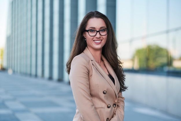 Portrait of a successful businesswoman with a charming smile posing on the street with interesting architecture at the background.