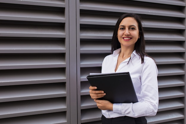 Portrait of successful young businesswoman standing with folder