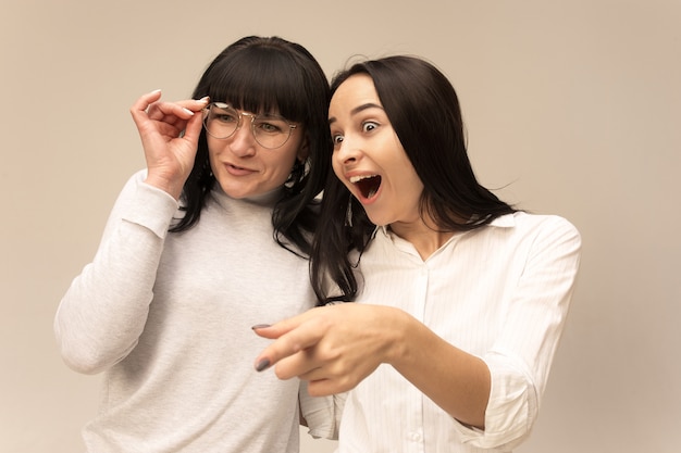 A portrait of a surprised happy mother and daughter at studio on gray