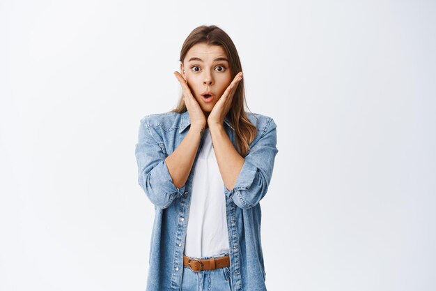 Portrait of surprised woman hear big news, gasping and touching face shocked, staring astonished, standing in casual clothes over white